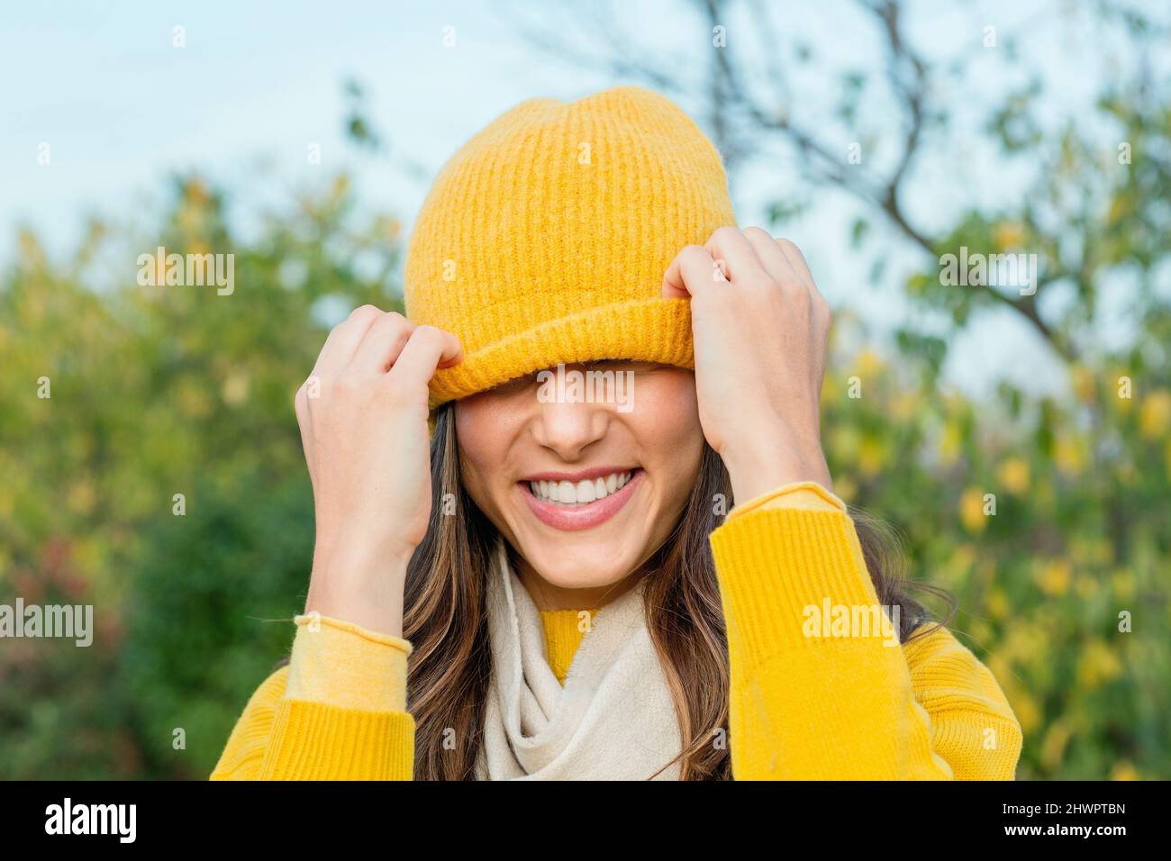 Happy young woman pulling down yellow knit hat Stock Photo Alamy