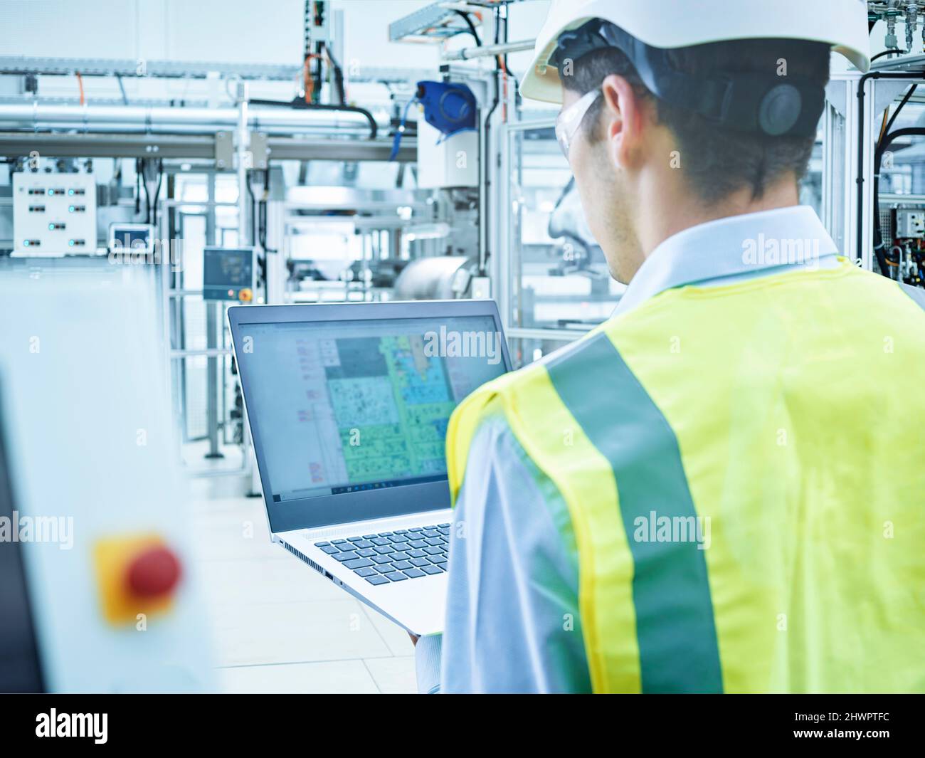 Young engineer in protective workwear using laptop at factory Stock Photo