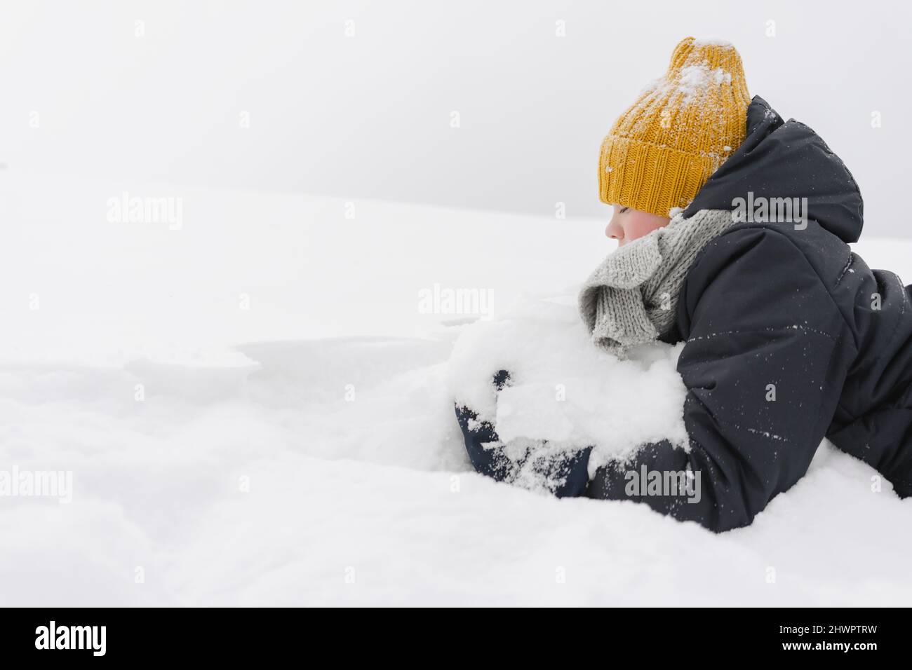 Boy wearing yellow knit hat playing with snow Stock Photo