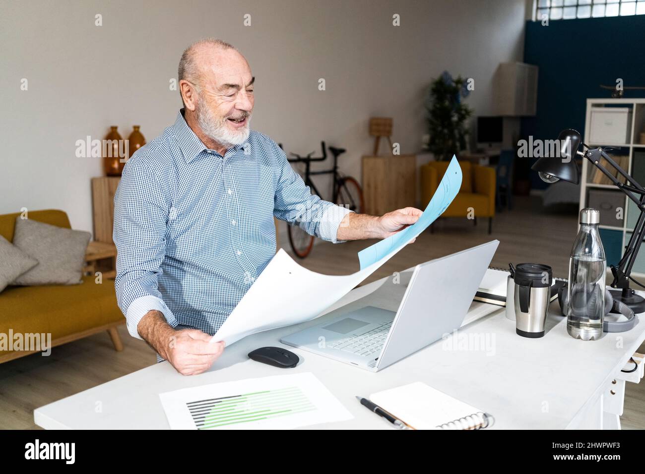 Smiling senior freelancer reading documents sitting in home office Stock Photo
