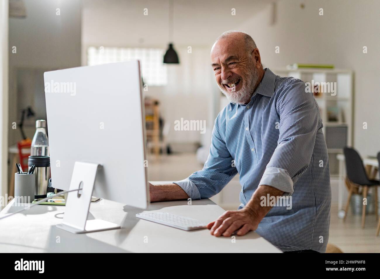 Cheerful senior freelancer with computer working from home Stock Photo