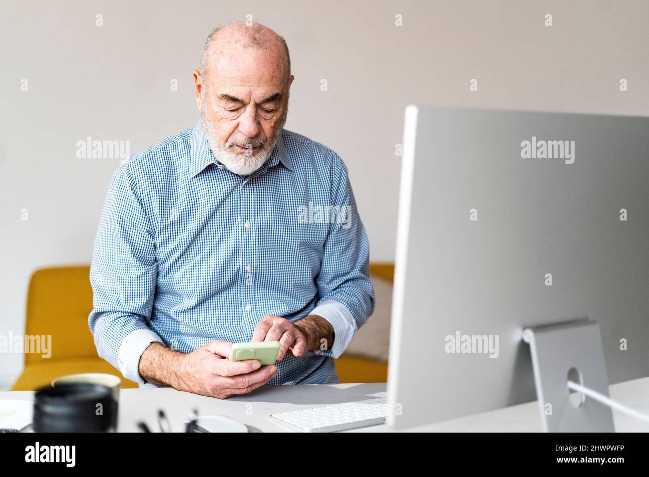 Freelancer text messaging through smart phone in home office Stock Photo