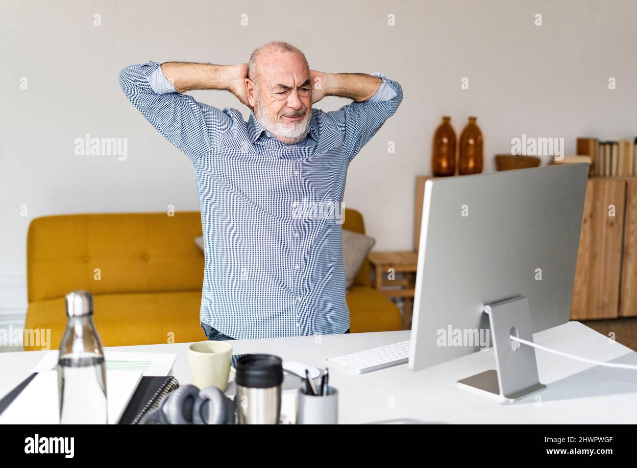 Tired freelancer with hands behind head sitting at desk Stock Photo