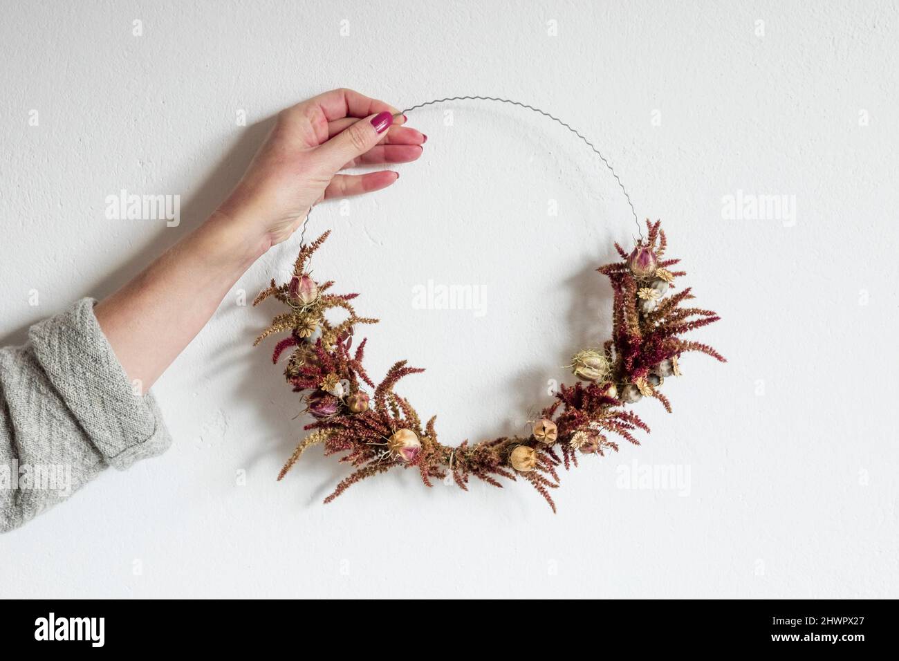 Arm of woman holding wreath made of various dried flowers Stock Photo