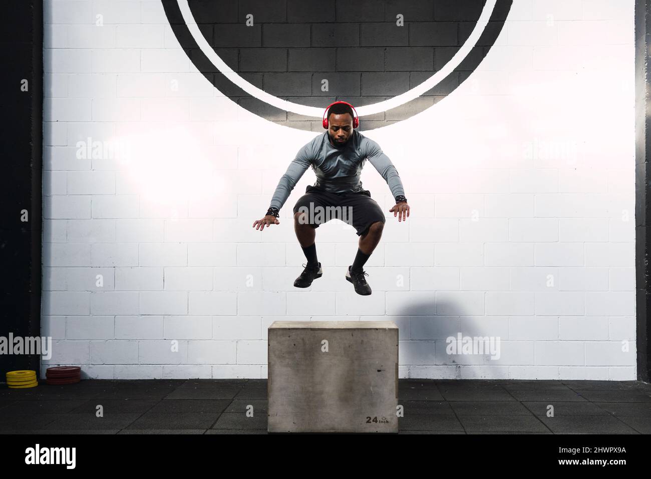 Young athlete practicing box squats in front of wall in gym Stock Photo