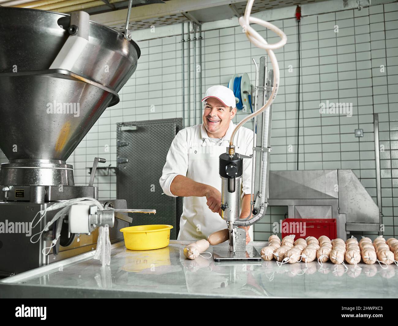 Happy butcher making sausages through machinery at factory Stock Photo