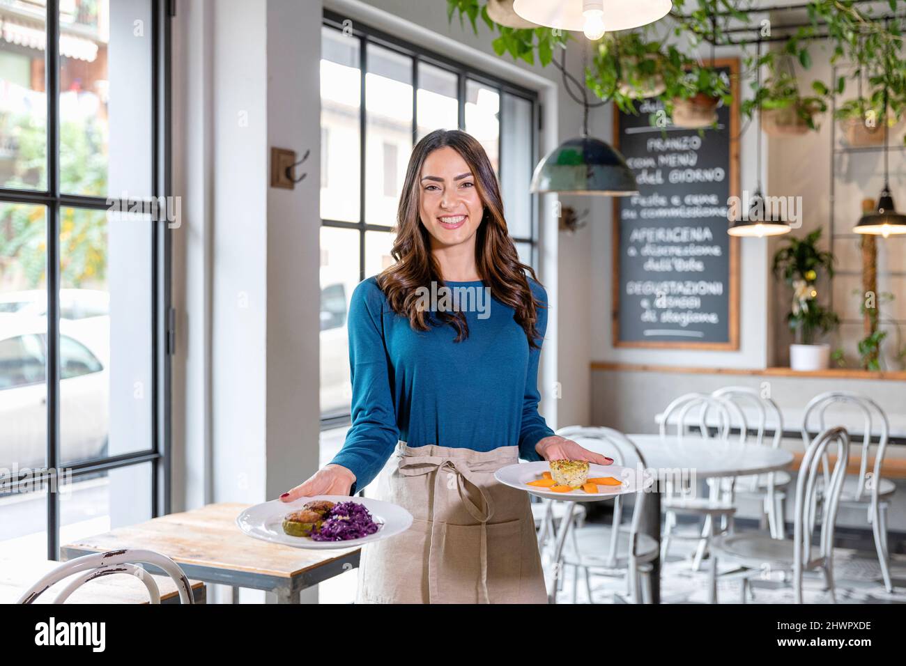 Smiling waitress carrying food plates in cafe Stock Photo