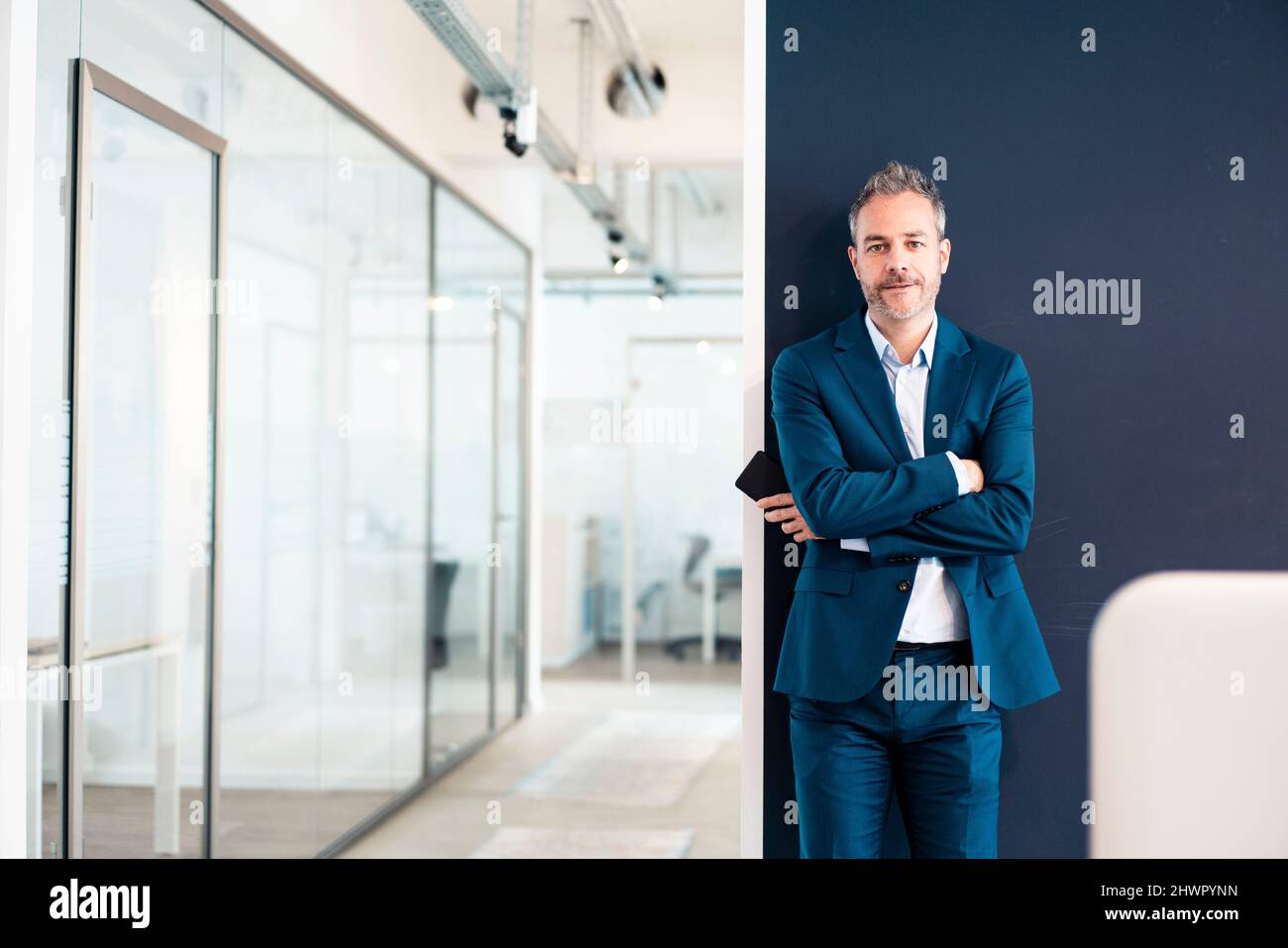 Confident businessman standing with arms crossed in office Stock Photo ...