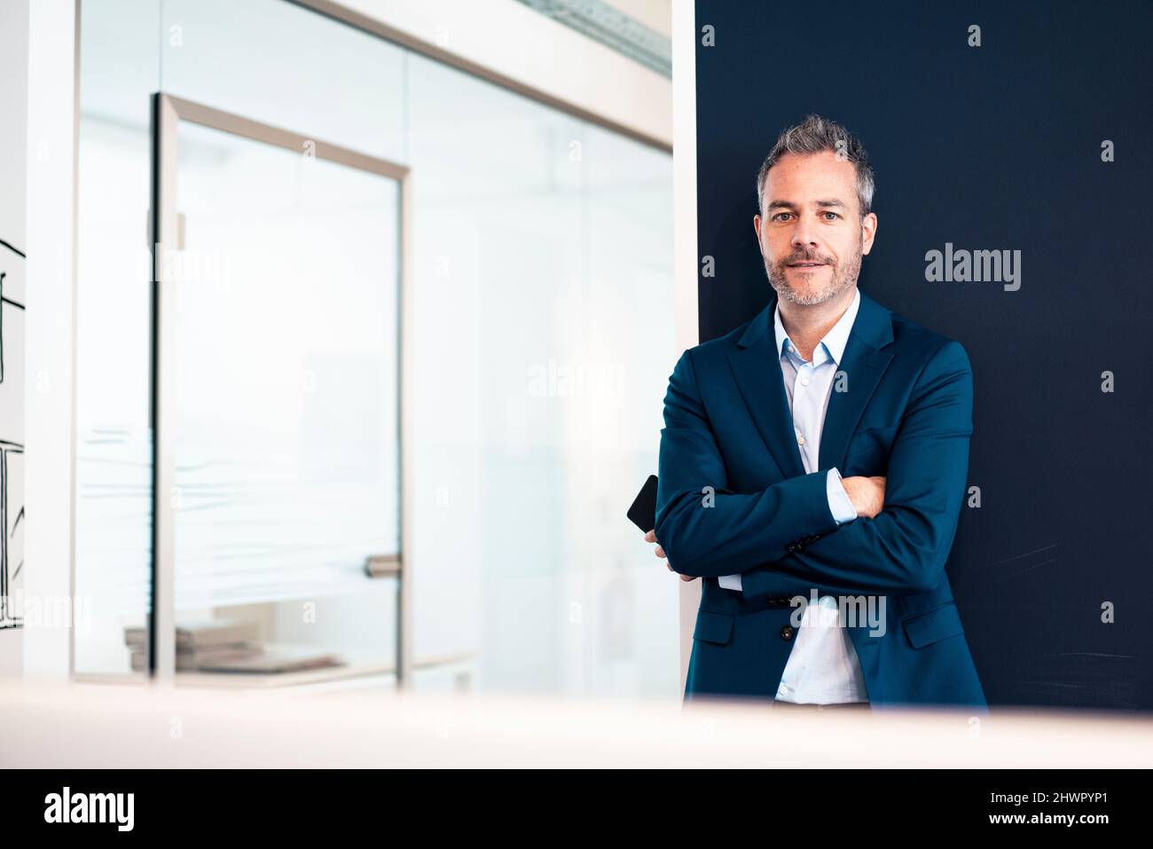 Confident businessman standing with arms crossed in office Stock Photo ...