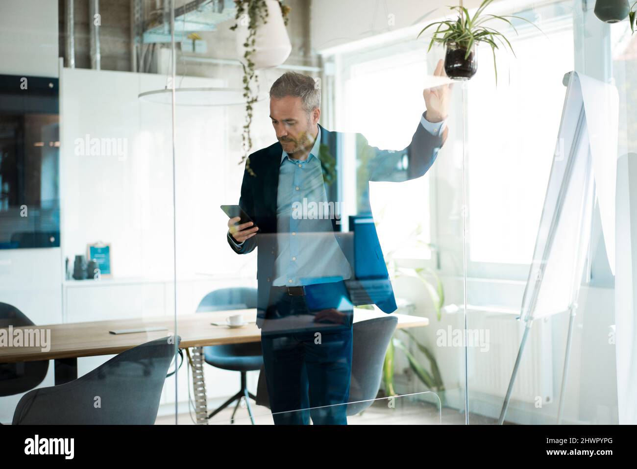 Businessman using tablet computer in meeting room seen through glass wall Stock Photo