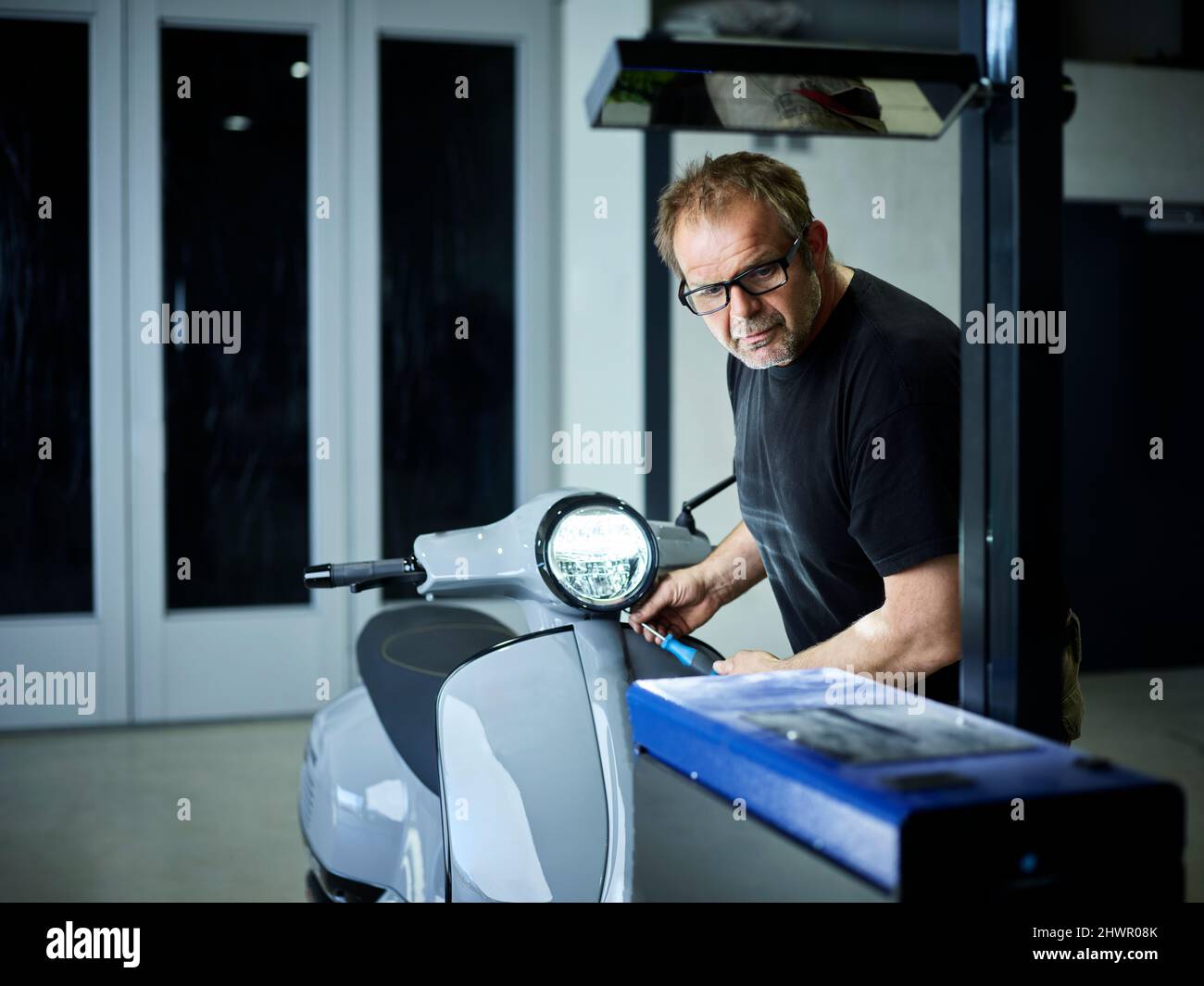 Mechanic adjusting headlight on motor scooter at auto repair shop Stock