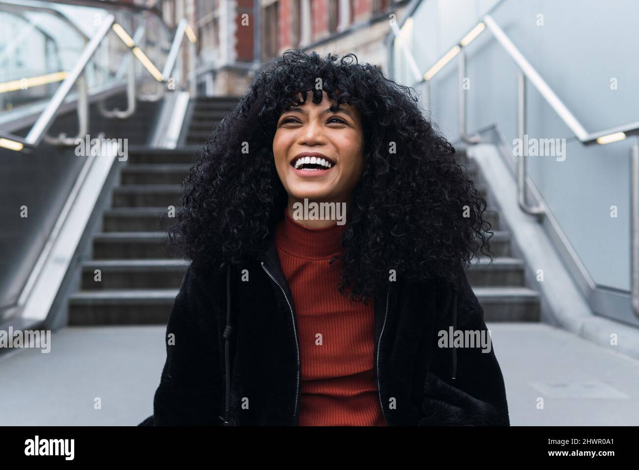 Happy young curly haired woman in front of staircase Stock Photo