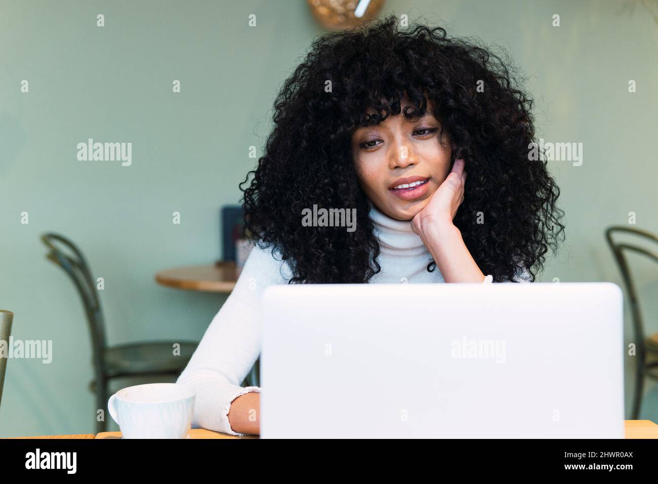 Curly black haired woman using laptop at cafe Stock Photo
