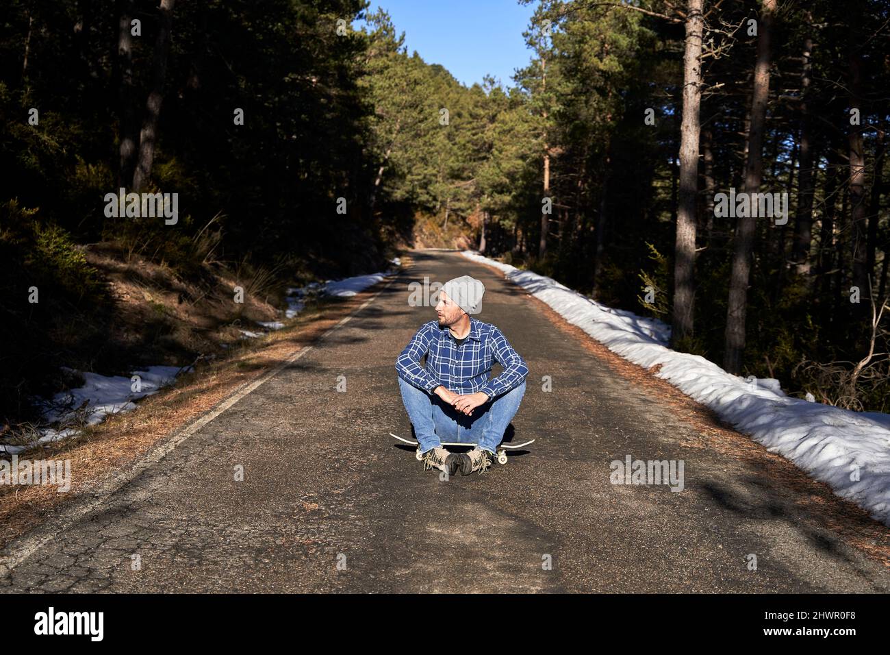 Man wearing knit hat sitting on skateboard Stock Photo