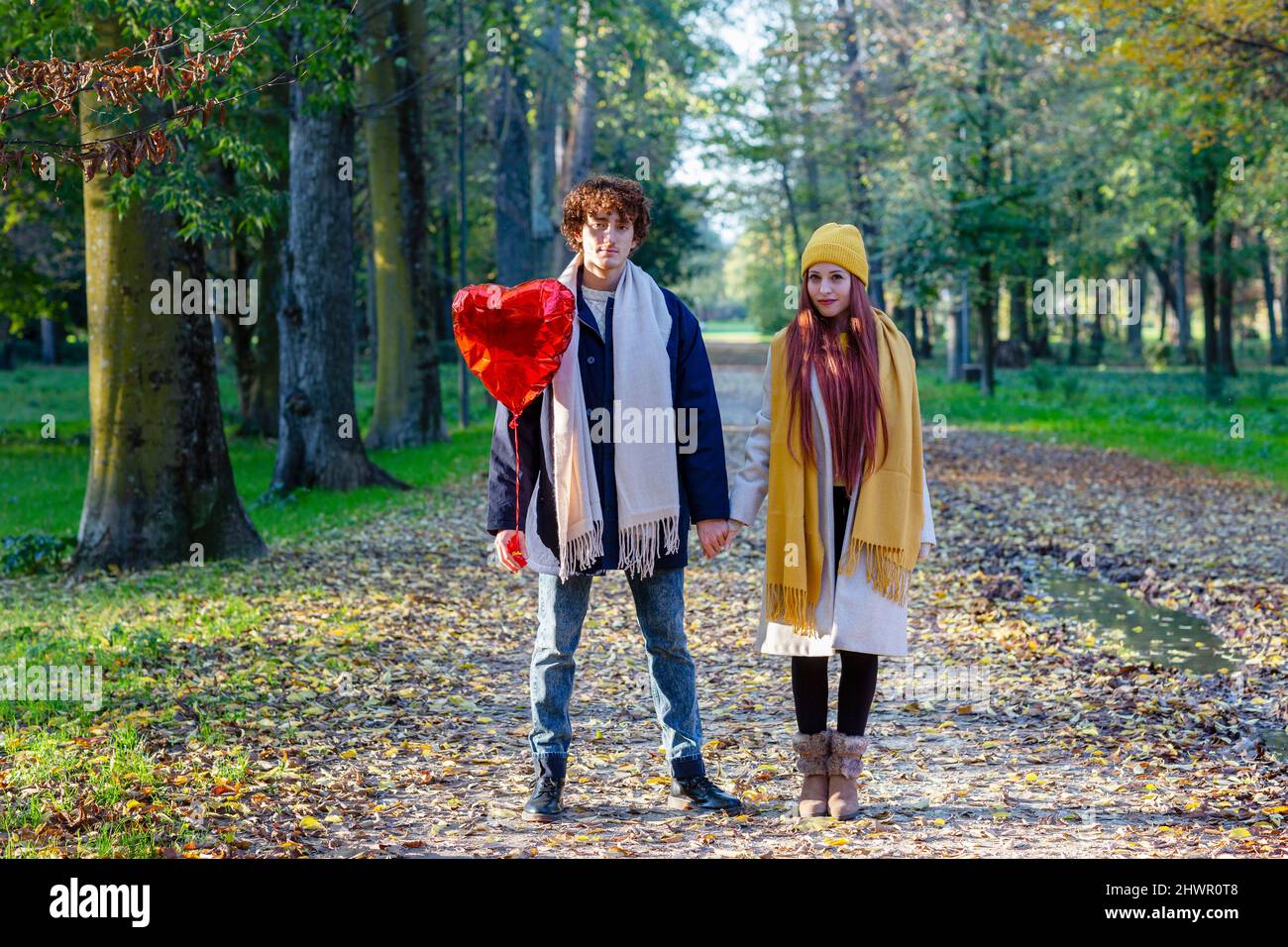 Couple holding hands standing with red heart shape balloon at park ...