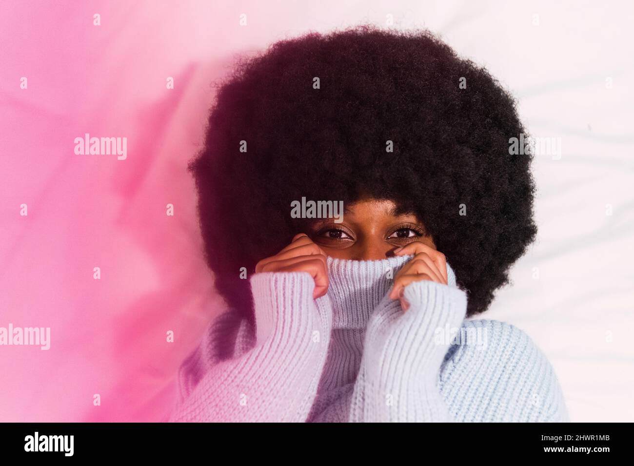 Afro young woman covering face with turtleneck sweater Stock Photo