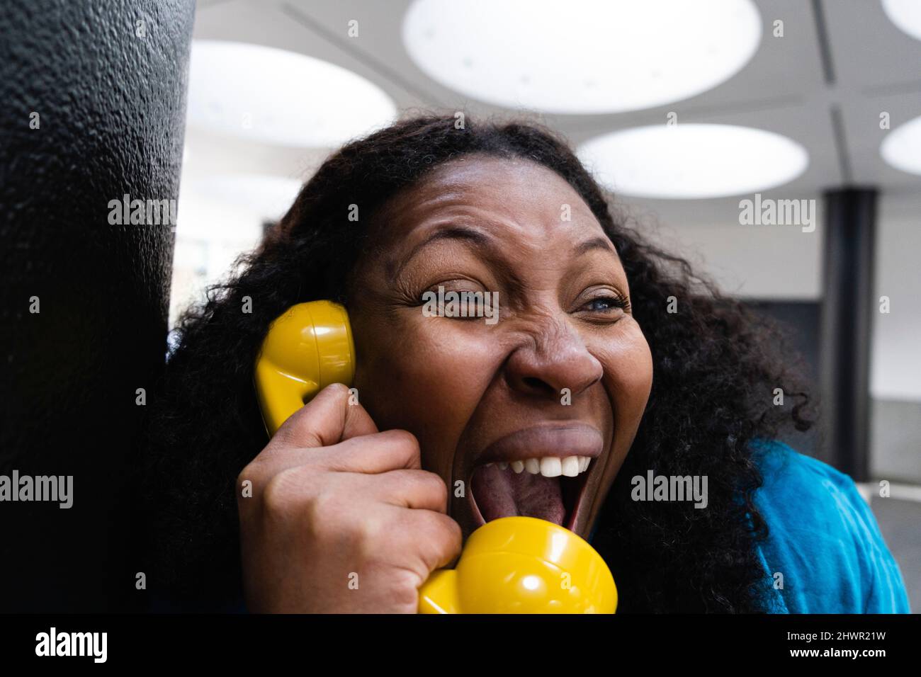 Happy woman listening through old-fashioned yellow telephone receiver Stock Photo