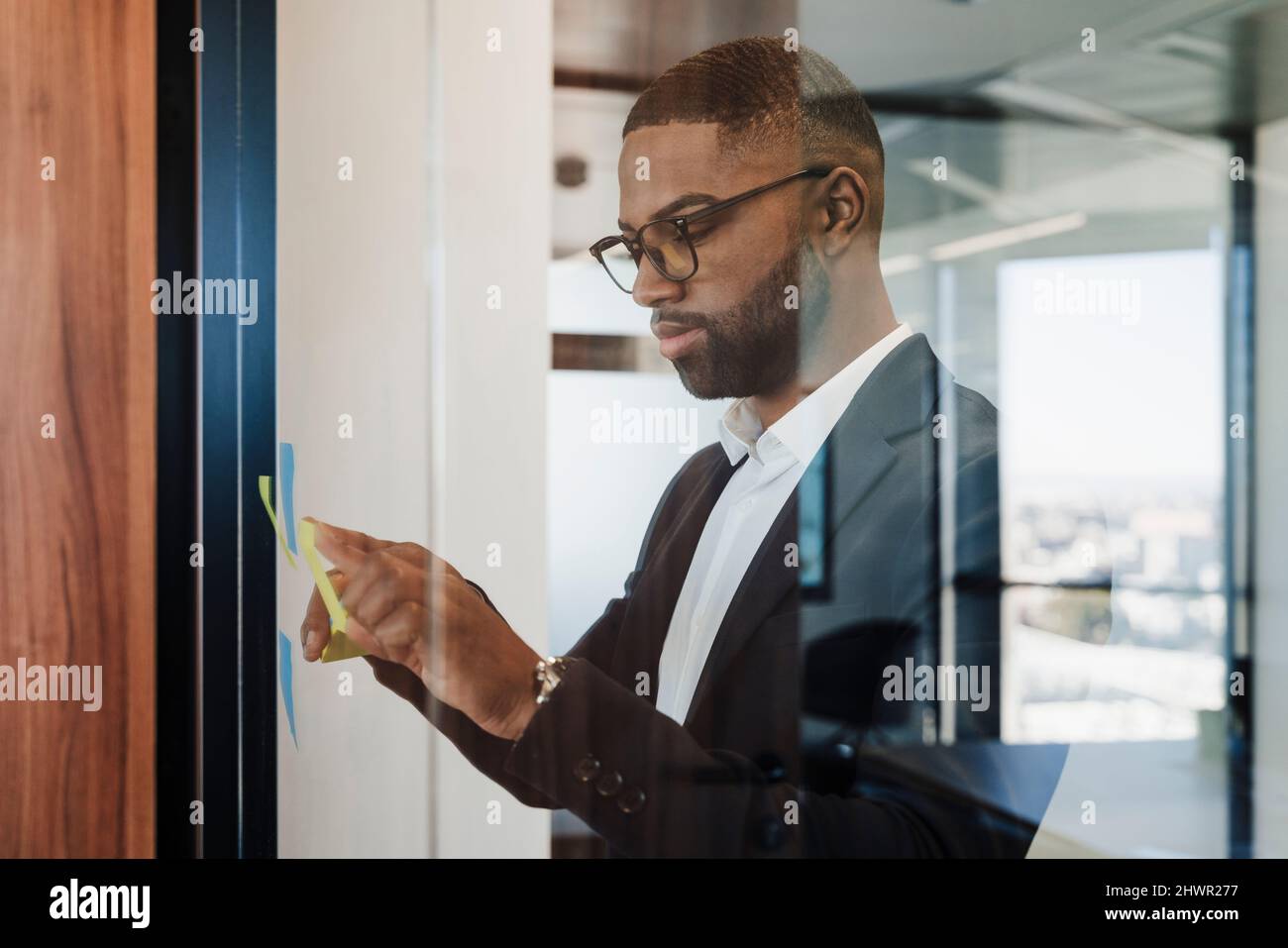Businessman sticking adhesive note on glass wall at office Stock Photo