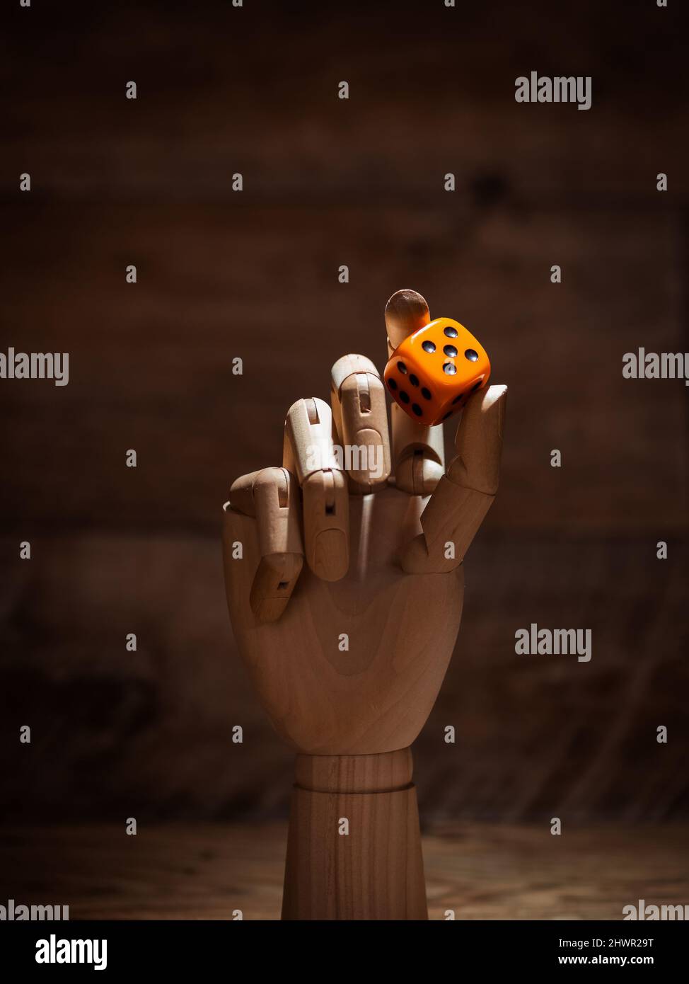 Wooden hand of mannequin holding a dice on wooden background with copy space, vertical photo Stock Photo