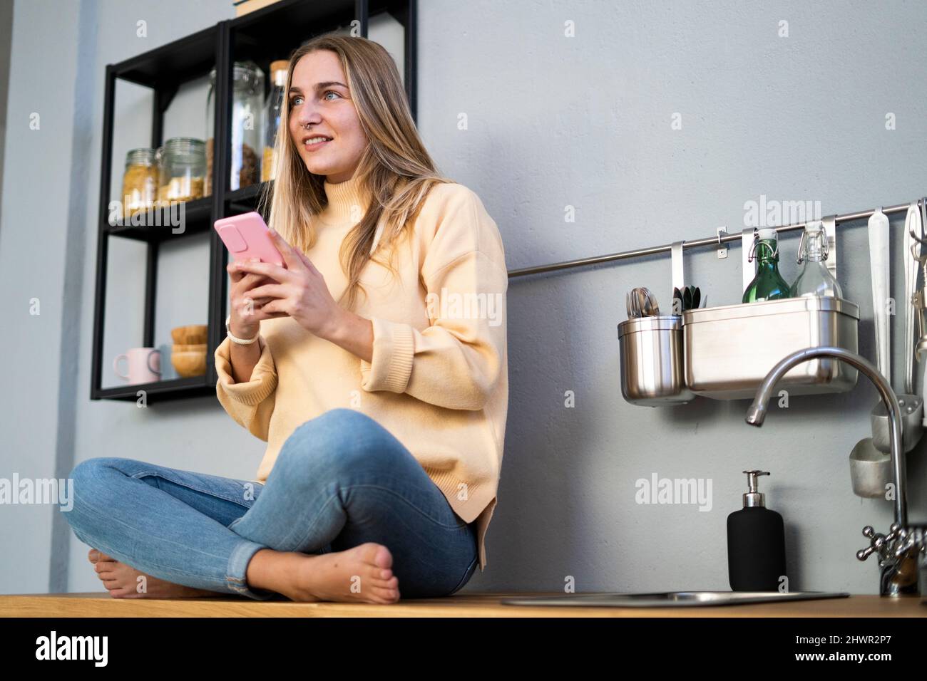 Contemplative woman with smart phone in kitchen Stock Photo