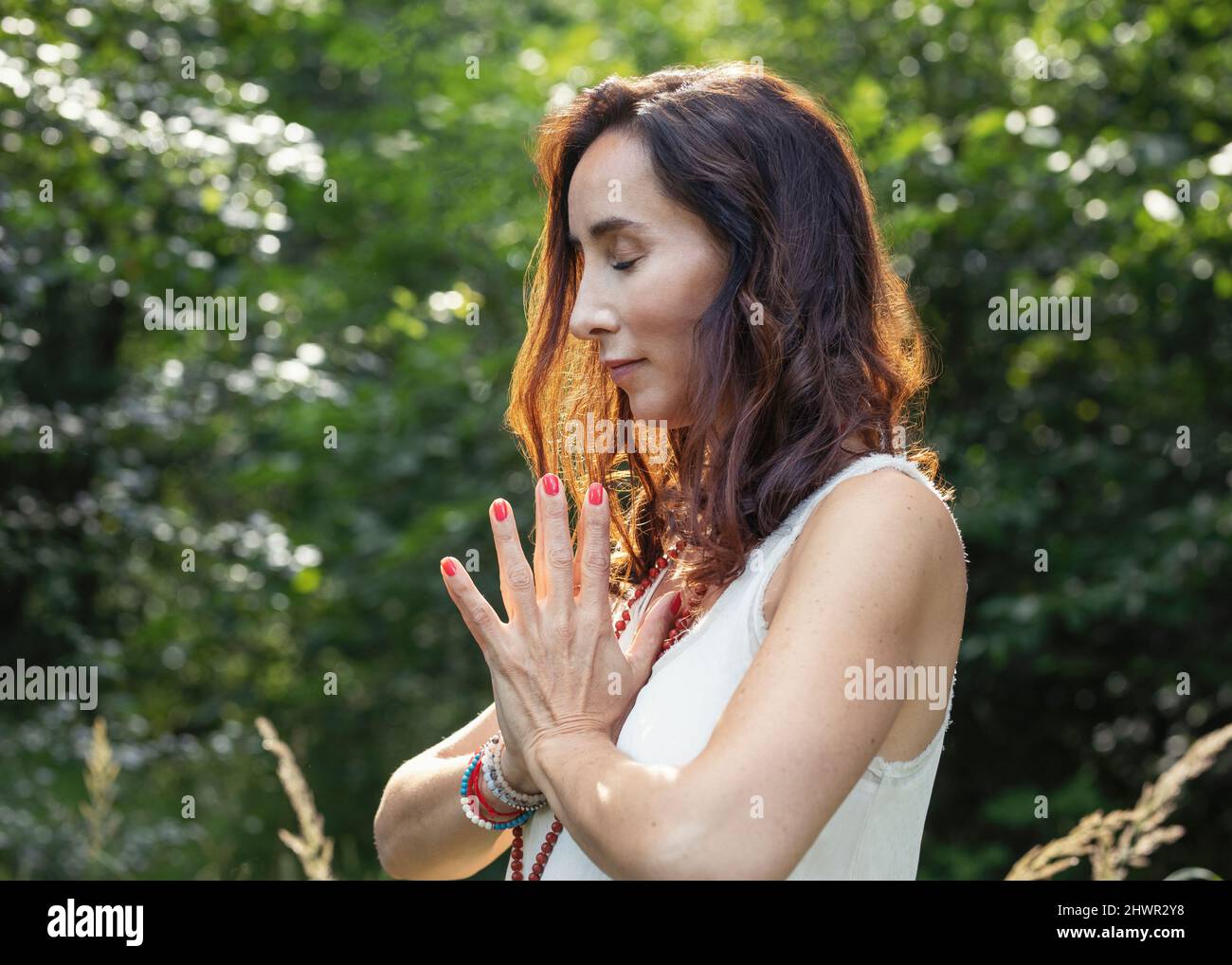 Woman with eyes closed and hands clasped meditating in nature Stock Photo