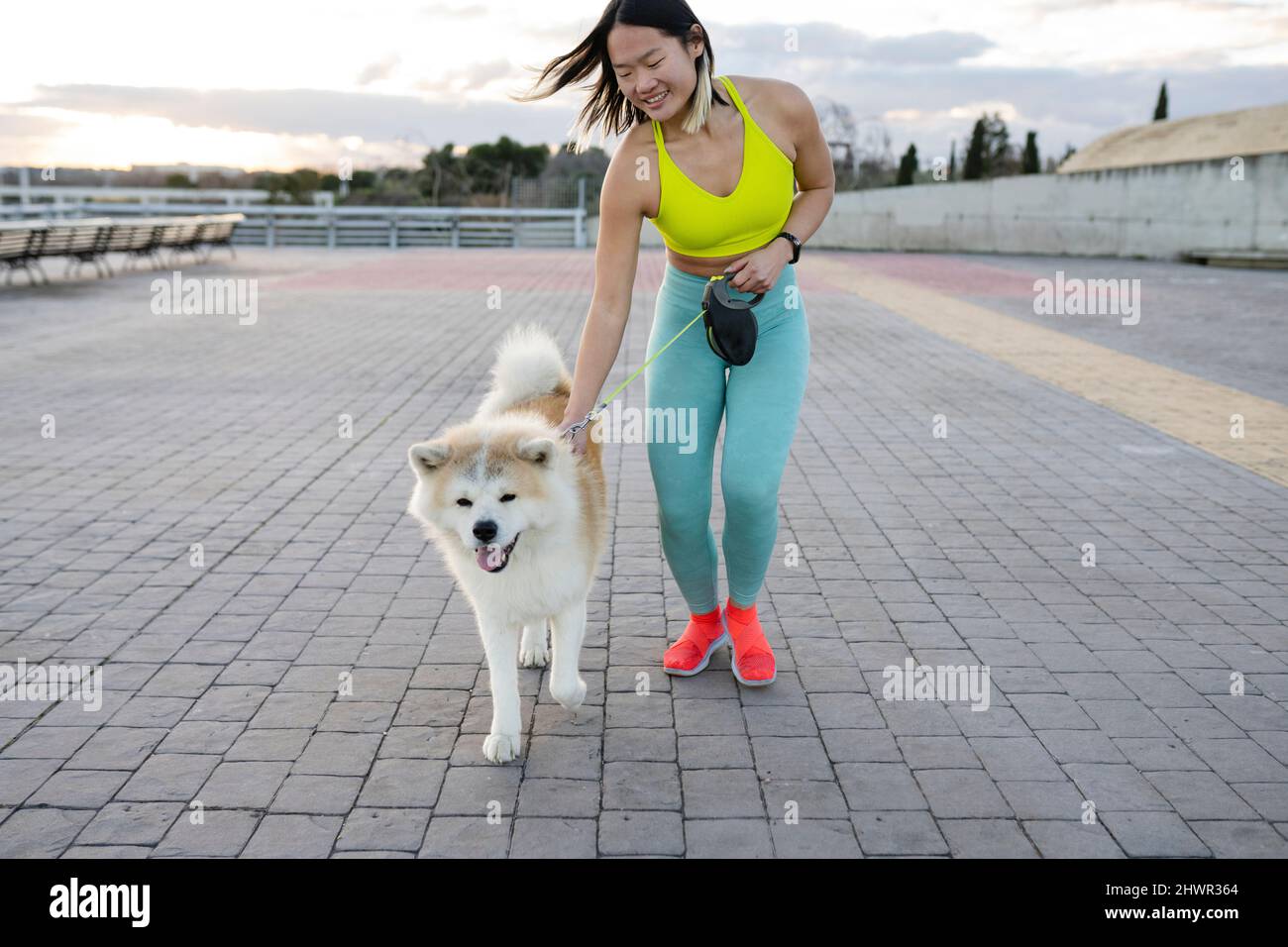 Smiling sportswoman dog walking on footpath Stock Photo