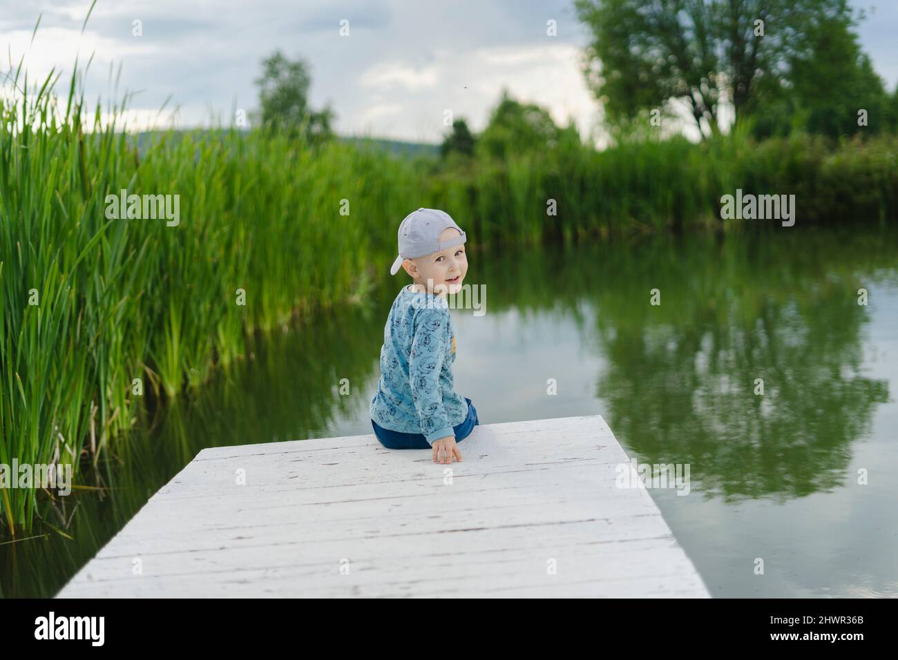 boy-looking-over-shoulder-sitting-on-jetty-by-lake-stock-photo-alamy