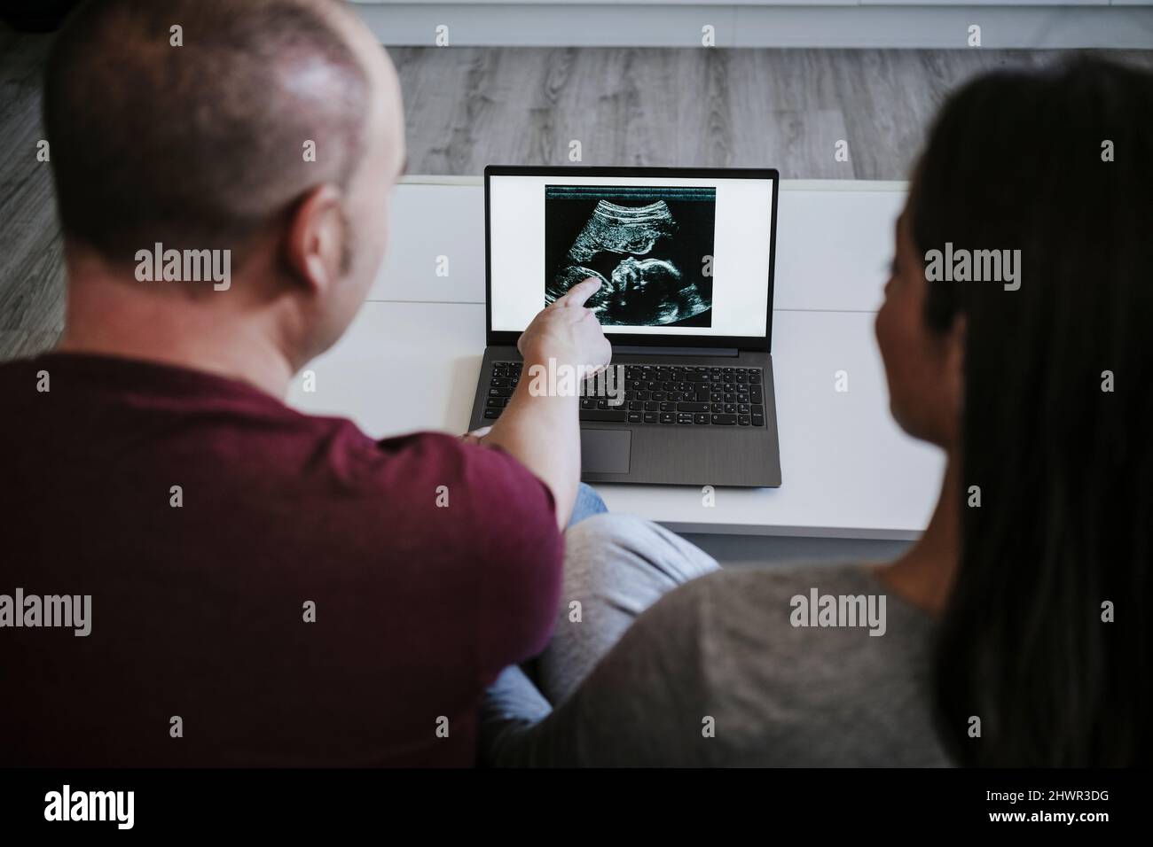 Man explaining ultrasound to pregnant woman on laptop at home Stock Photo