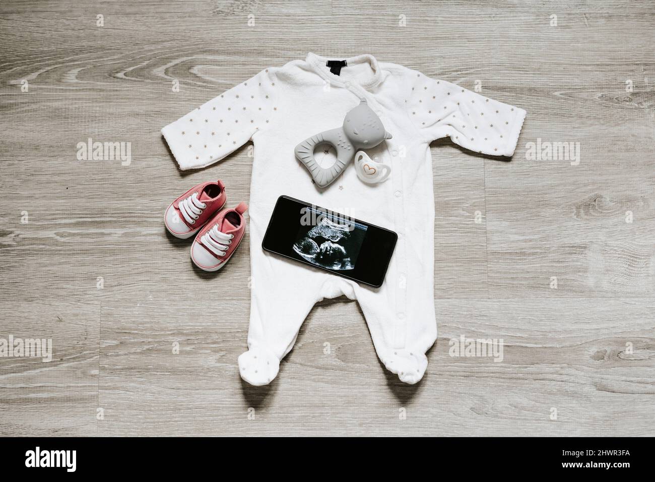 Baby clothing and pacifier with ultrasound image on smart phone at home Stock Photo