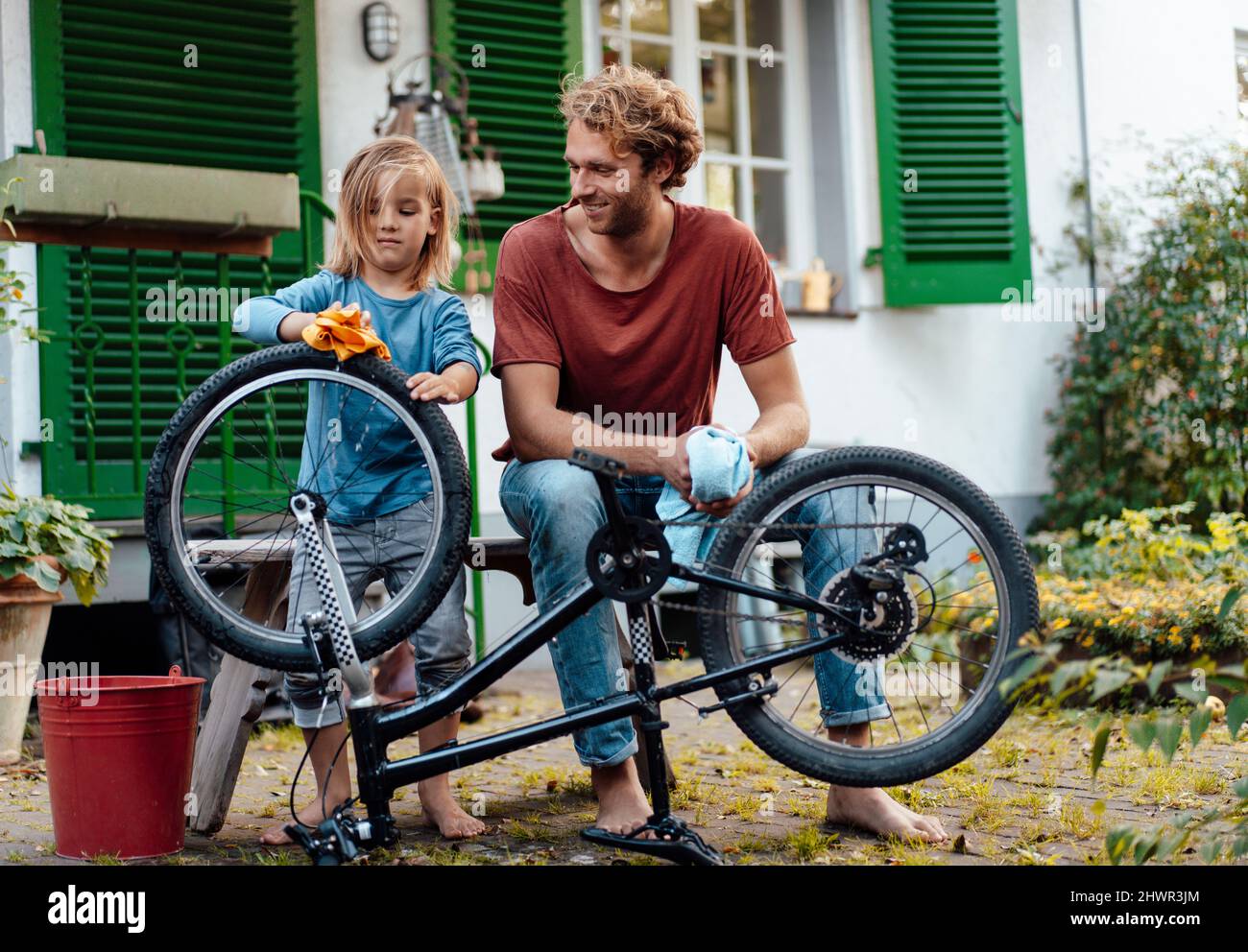 Boy cleaning bicycle by father in backyard Stock Photo Alamy
