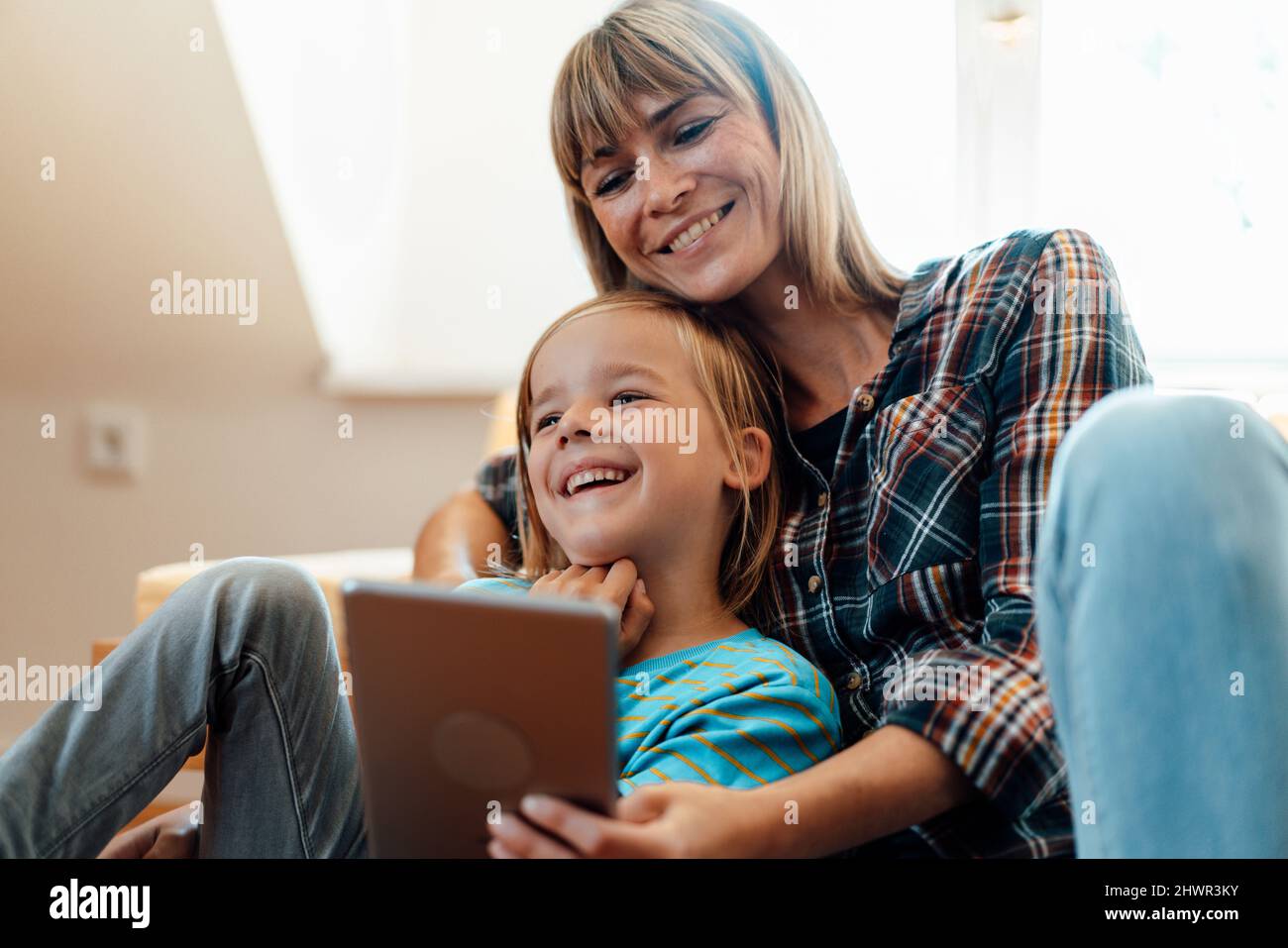 Son laughing by mother using tablet PC at home Stock Photo