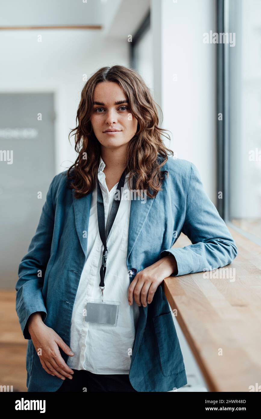 Businesswoman wearing ID card standing by desk in office Stock Photo