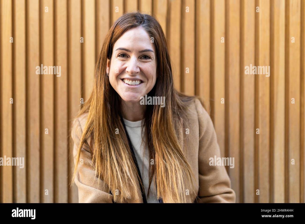 Happy woman with long brown hair in front of wall Stock Photo - Alamy