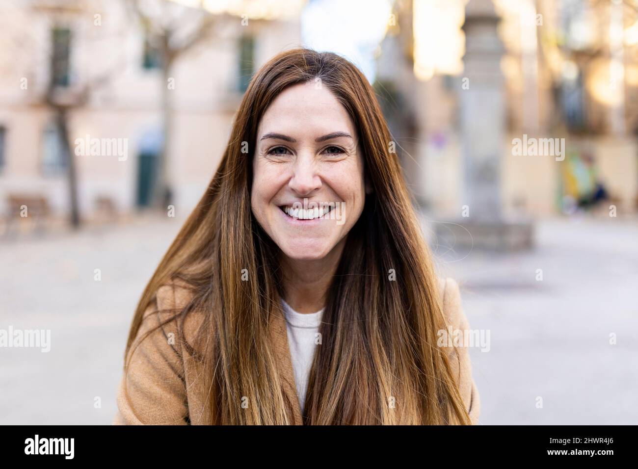 Happy woman with long brown hair in city Stock Photo