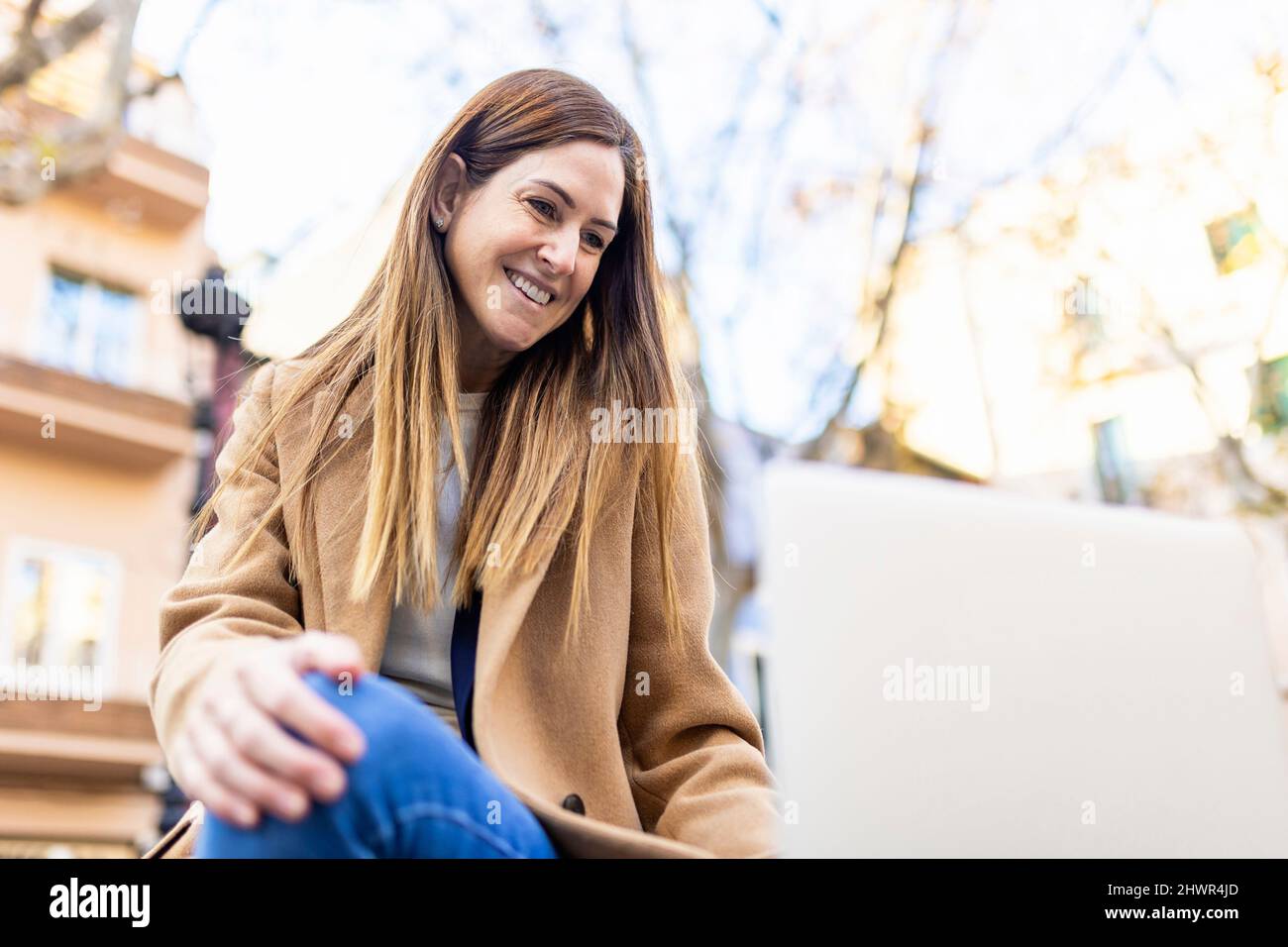 Smiling woman with brown hair looking at laptop in city Stock Photo