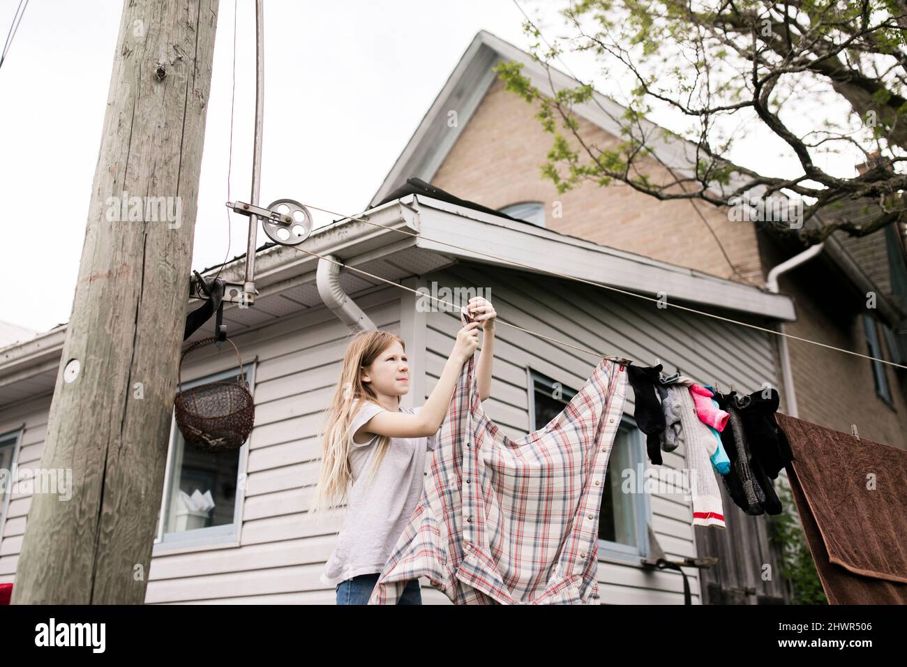 Girl hanging clothes on rope outside house Stock Photo