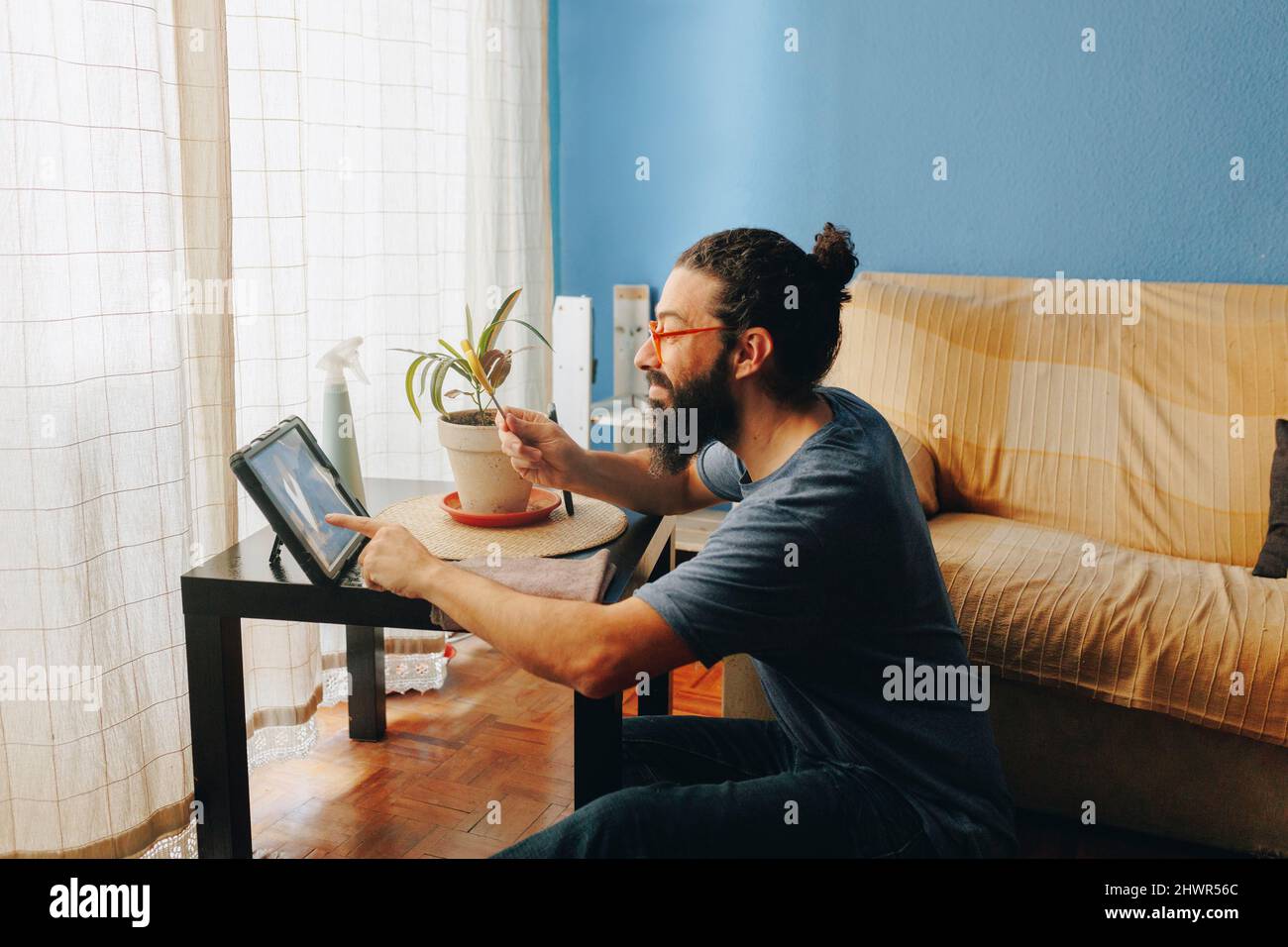 Man showing scissors on video call through tablet PC sitting by sofa at home Stock Photo
