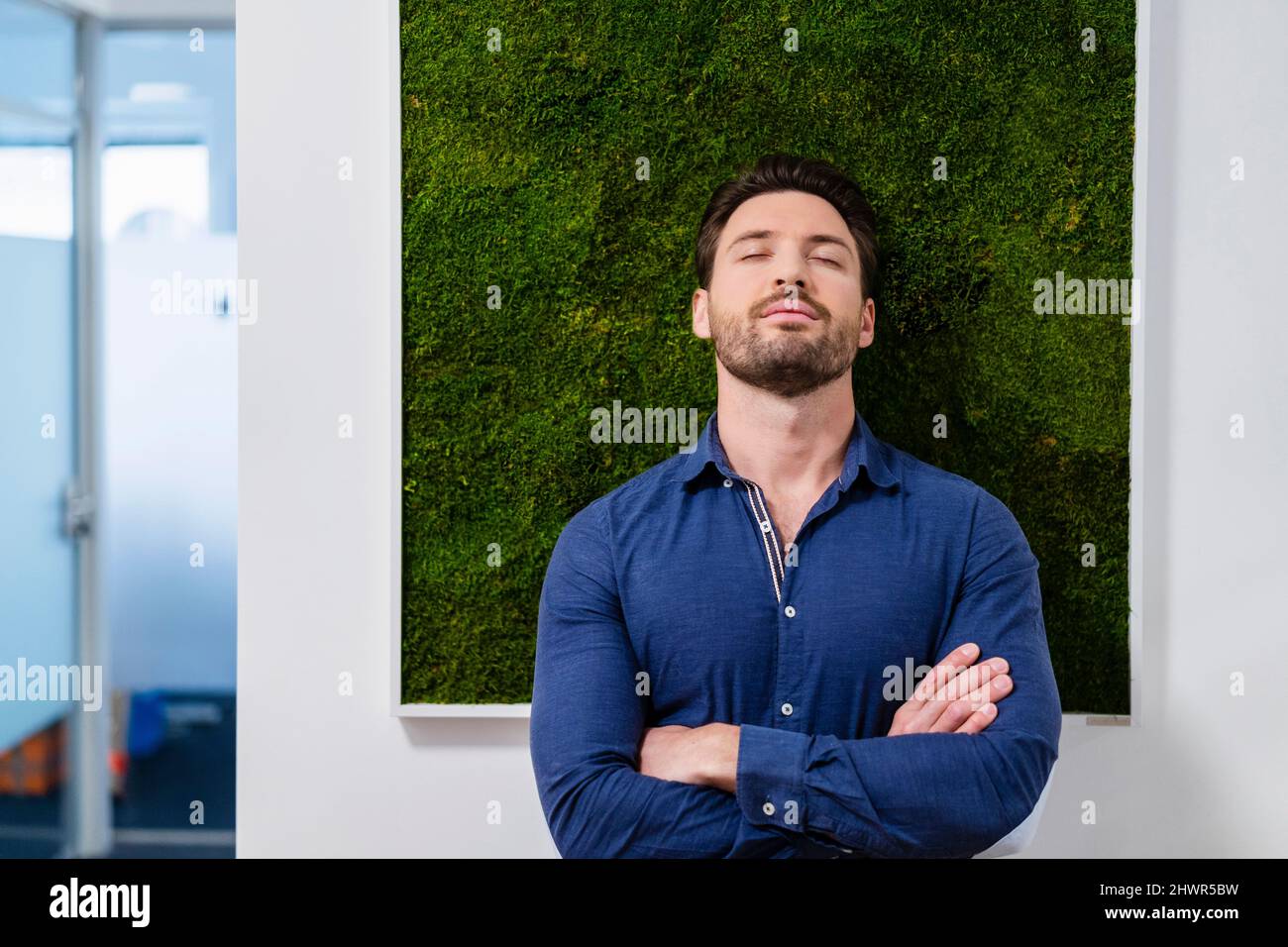 Businessman with arms crossed in front of wall at office Stock Photo ...