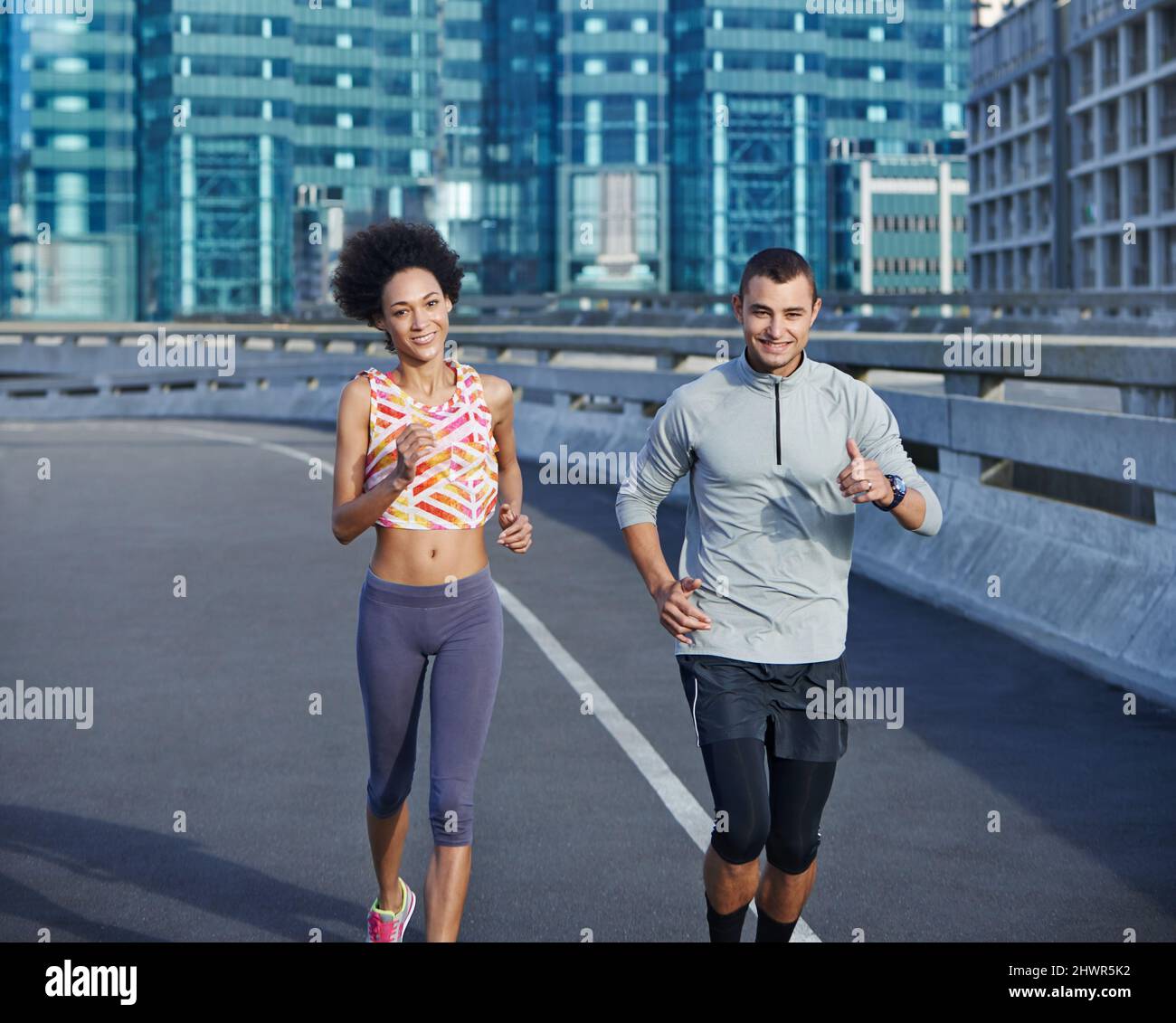 We love a bit of competition. Shot of two friends jogging together through the city streets. Stock Photo