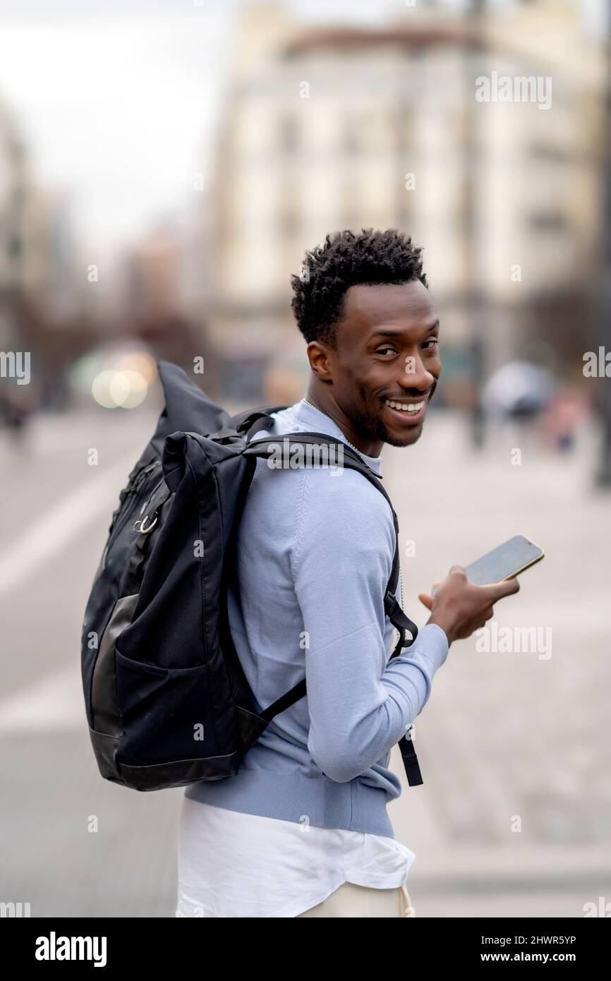 Smiling young man with backpack holding mobile phone Stock Photo