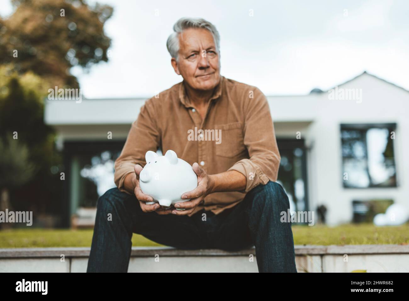 Senior man with white hair holding piggy bank at backyard Stock Photo