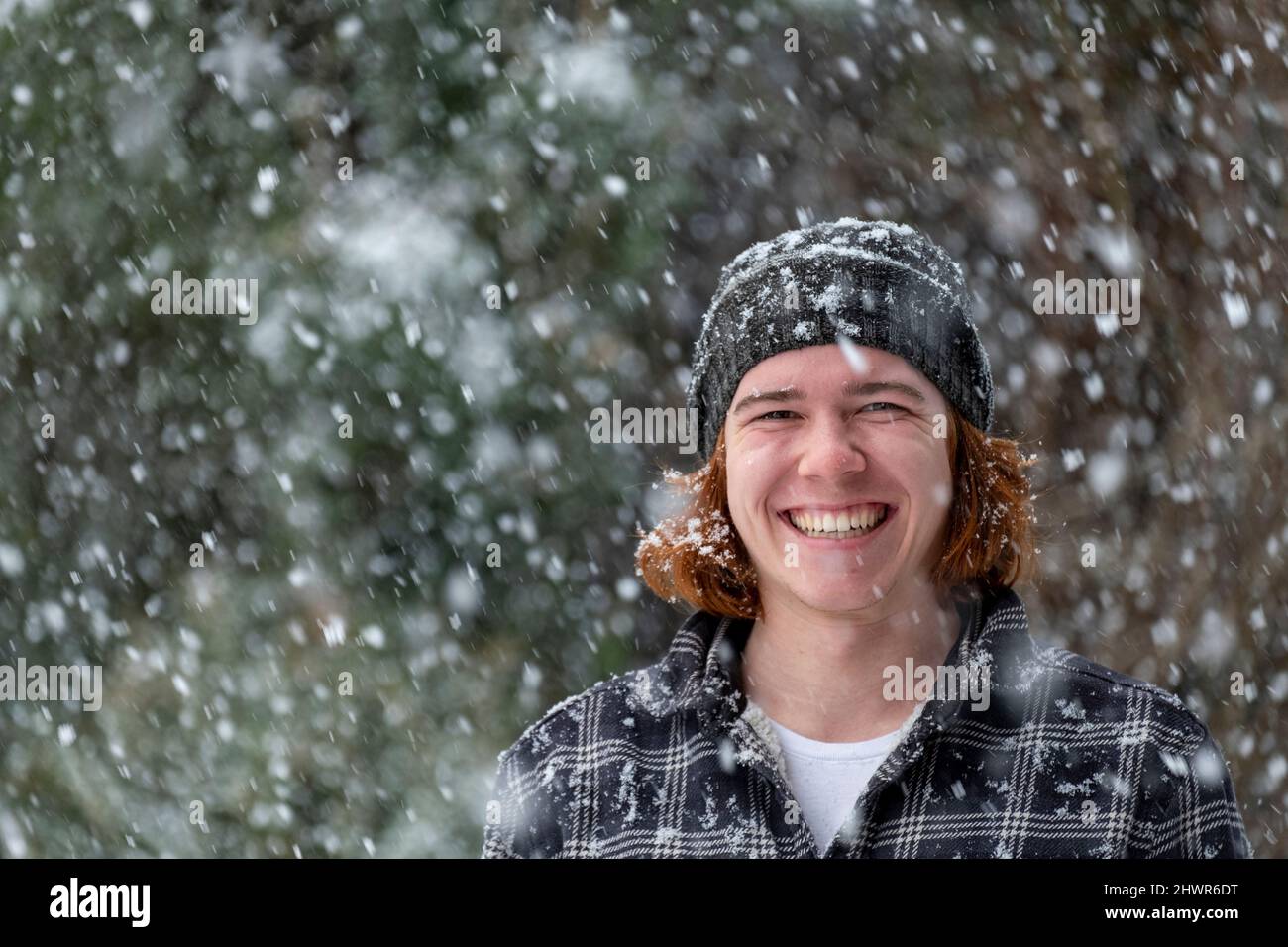 Smiling young man in knit hat enjoying snowfall Stock Photo