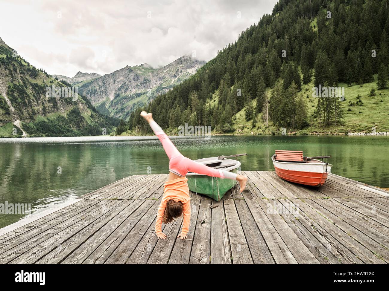 Girl doing cartwheel on jetty by lake Stock Photo