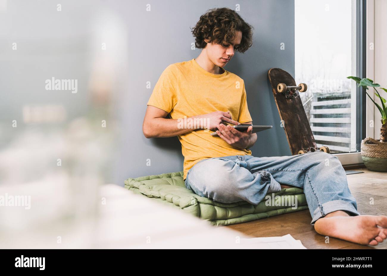 Young man using tablet PC by skateboard at home Stock Photo