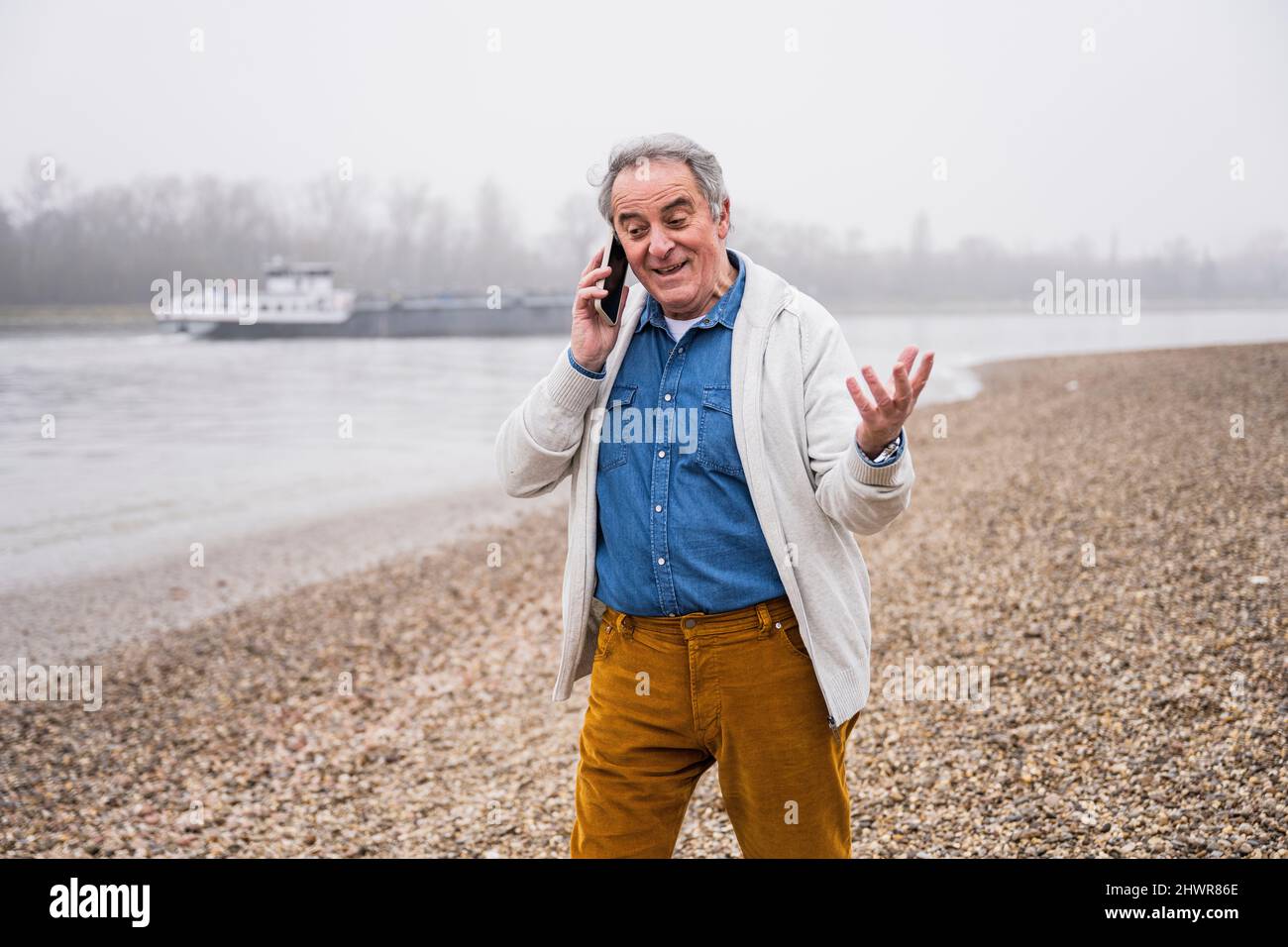 Senior man talking on mobile phone gesturing at beach Stock Photo