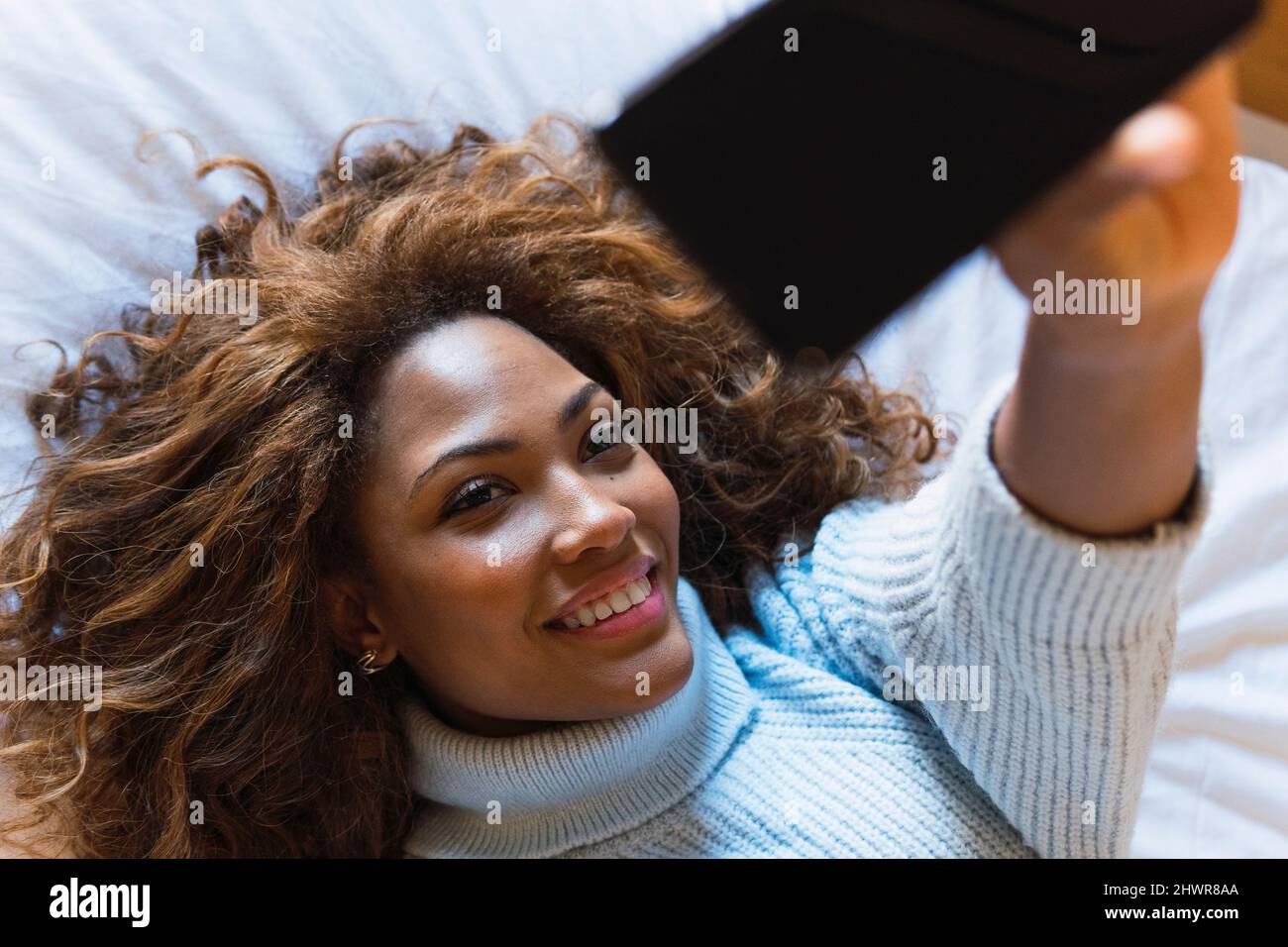 Young woman taking selfie through smart phone lying on bed at home Stock Photo