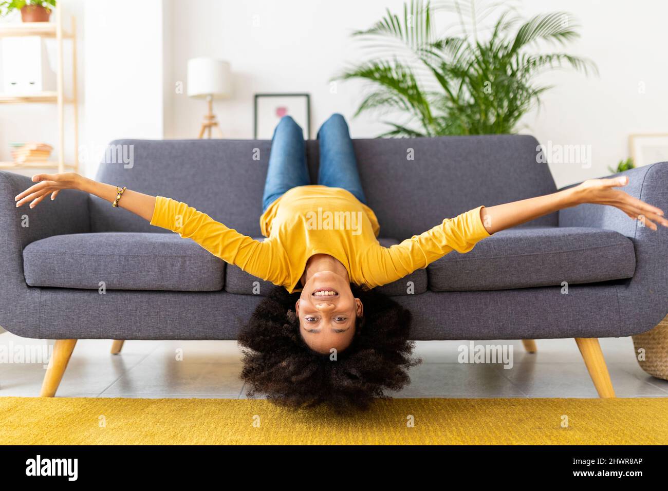 Happy young woman lying upside down on sofa in living room at home