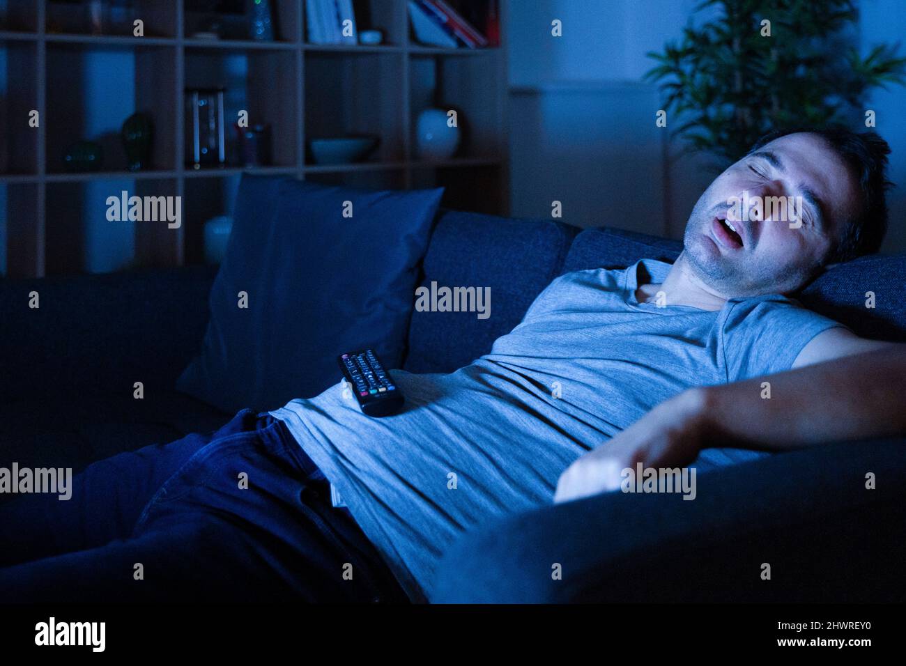 Tired man sleeping at night on the sofa watching tv at home Stock Photo