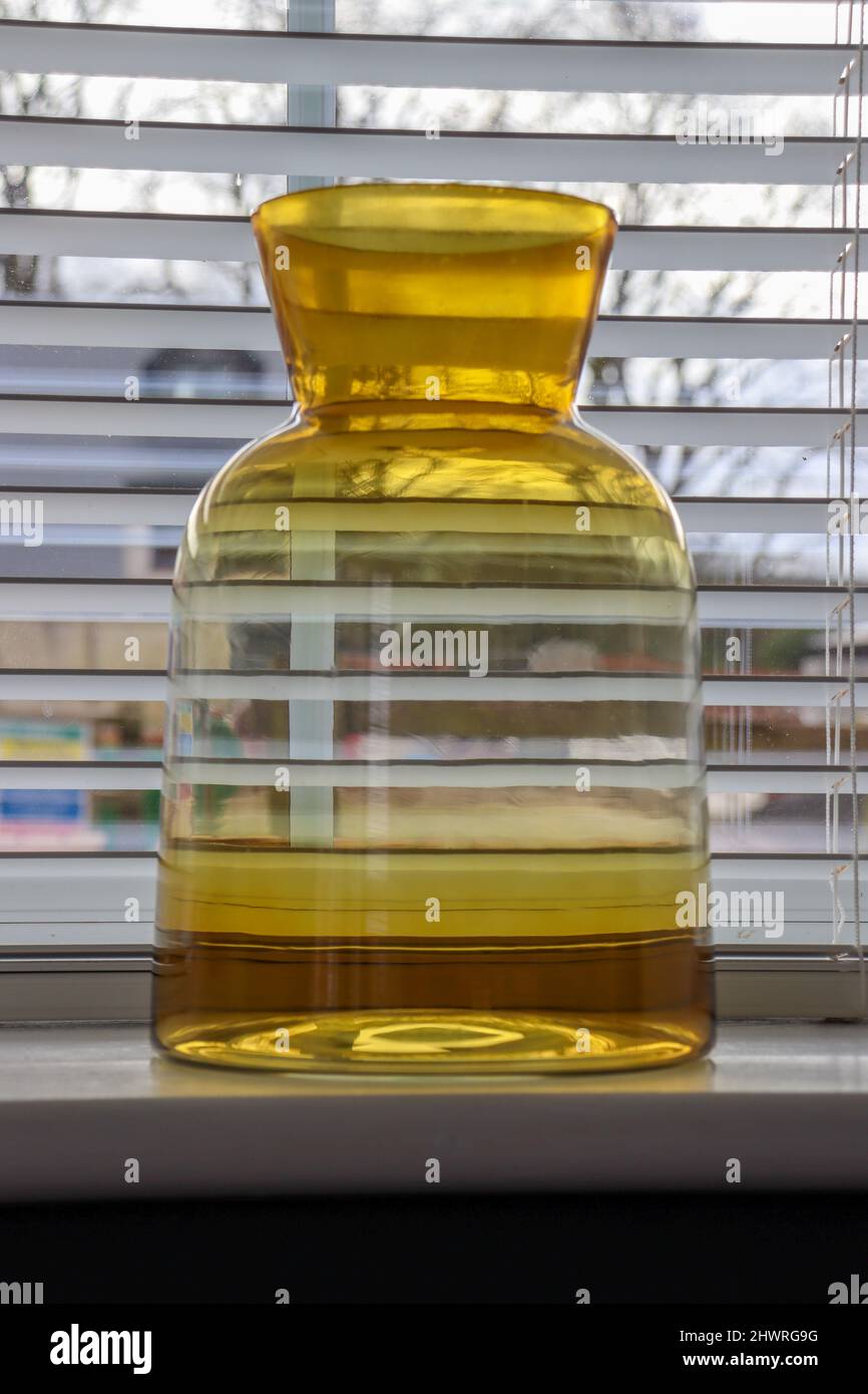 Yellow transparent yellow / ochre ombre vase on window ledge / sill Stock Photo