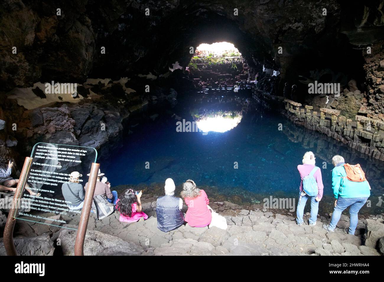tourists sit on edge of lava tunnel with saltwater lagoon lake in jameos del agua lanzarote, canary islands, spain the white spots are the unique blin Stock Photo
